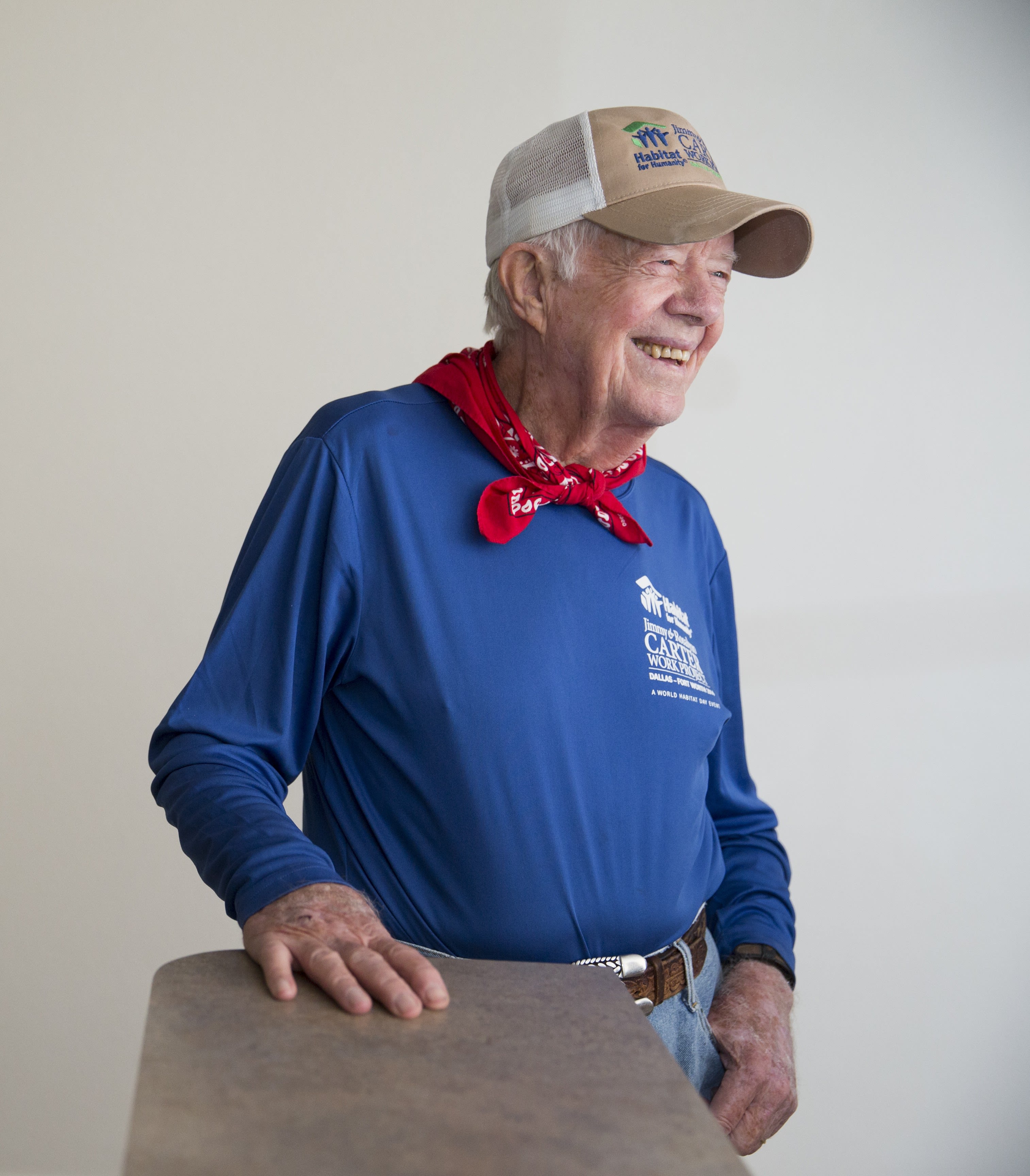 Jimmy Carter, a man in a blue shirt with red handkerchief around neck and wearing a Habitat branded baseball cap, smiling